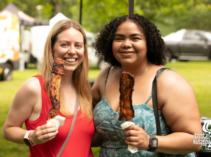 2 women women posing with bacon on a stick from a food vendor at an outdoor wine and beer tasting festival in Kutztown Pennsylvania