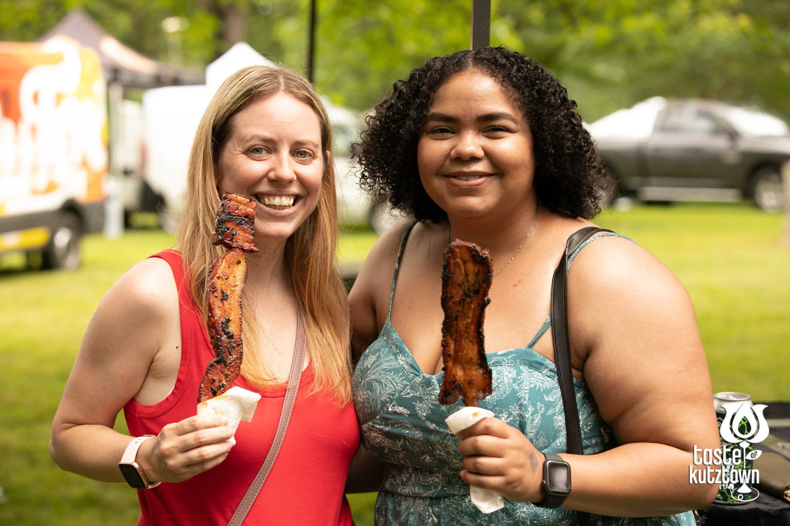 2 women women posing with bacon on a stick from a food vendor at an outdoor wine and beer tasting festival in Kutztown Pennsylvania